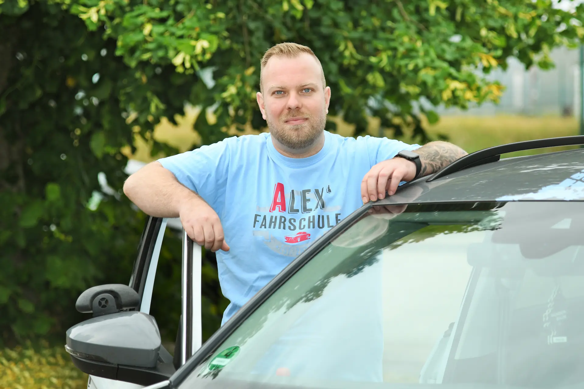 Philip, Fahrlehrer in Ausbildung, stehend an der Autotür eines Fahrschulautos